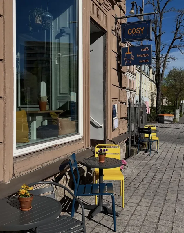 Außenansicht des cosy morning in der Bismarckstraße mit Tischen und gelben Stühlen in der Sonne